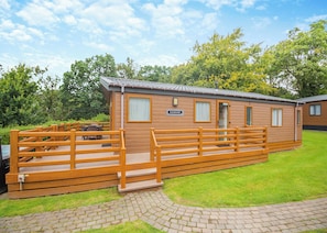 A wooden mobile home with a 'CLEANWATER' sign, a wooden deck, and a paved pathway. - Foxglove 6 Platinum (Pet) (Bala,)