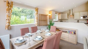 Een moderne keuken met houten kastjes, een eethoek met roze stoelen en uitzicht op groen.