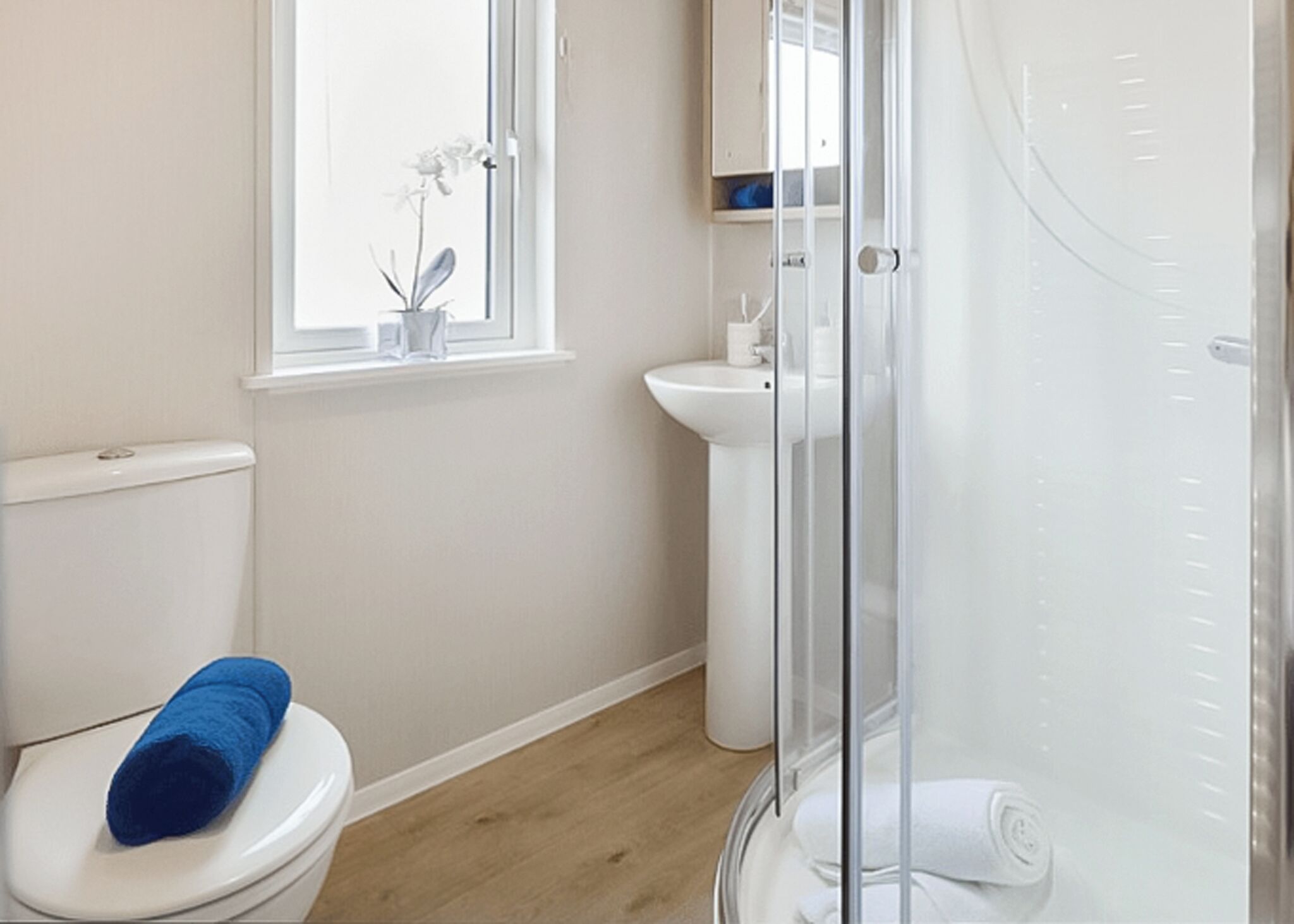 A bathroom with a toilet, a sink, a glass shower enclosure, and a window with a plant.