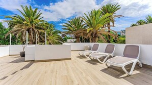 A rooftop terrace with palm trees, white lounge chairs, and a potted plant. - Palmera Sky Terrace Suite (Costa del Silencio)