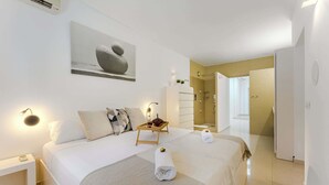 A hotel room with a large bed, a bedside table, a wall-mounted artwork, a bedside lamp, and a bathroom visible through an open door. - Palmera Sky Terrace Suite (Costa del Silencio)