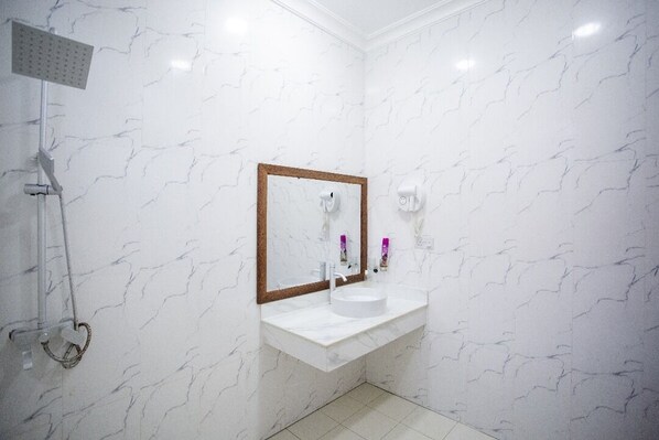 Un bagno con una parete in marmo bianco, un lavabo bianco con specchio a cornice in legno, un soffione a mano e due asciugacapelli fissati alla parete.