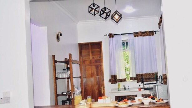 A kitchen with a wooden counter, a dining area with chairs, and a window with curtains. - Michamvi Holiday Homes (Michamvi)