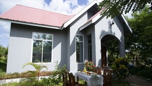 A house with a red roof, white walls, and a covered porch with a table set for a meal. - Michamvi Holiday Homes (Michamvi)