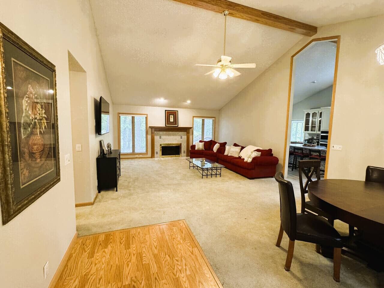 A spacious living room with a fireplace, a red sofa, a dining table with chairs, and a ceiling fan.