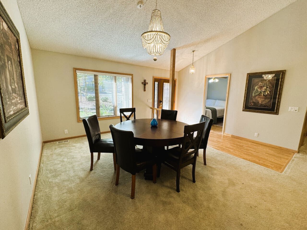 A dining area with a round table and chairs, a chandelier, and a cross on the wall.