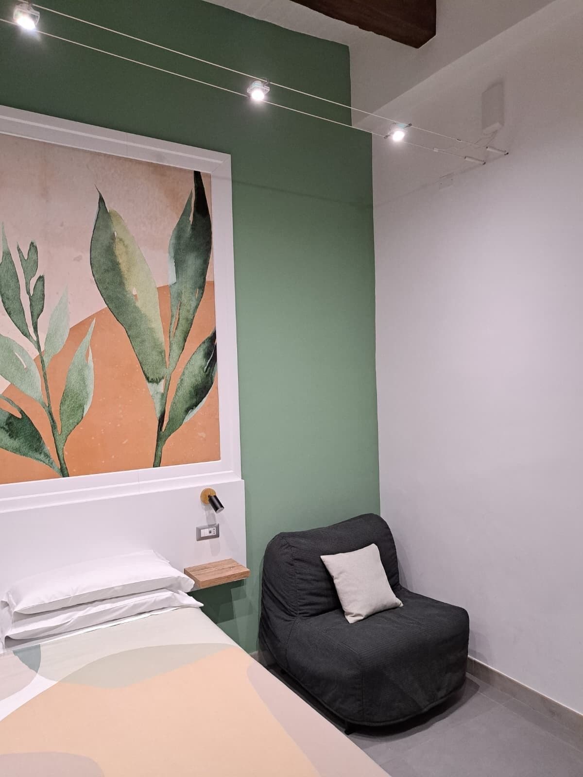 Une pièce avec un lit, une chaise, un grand tableau abstrait et un mur vert.
