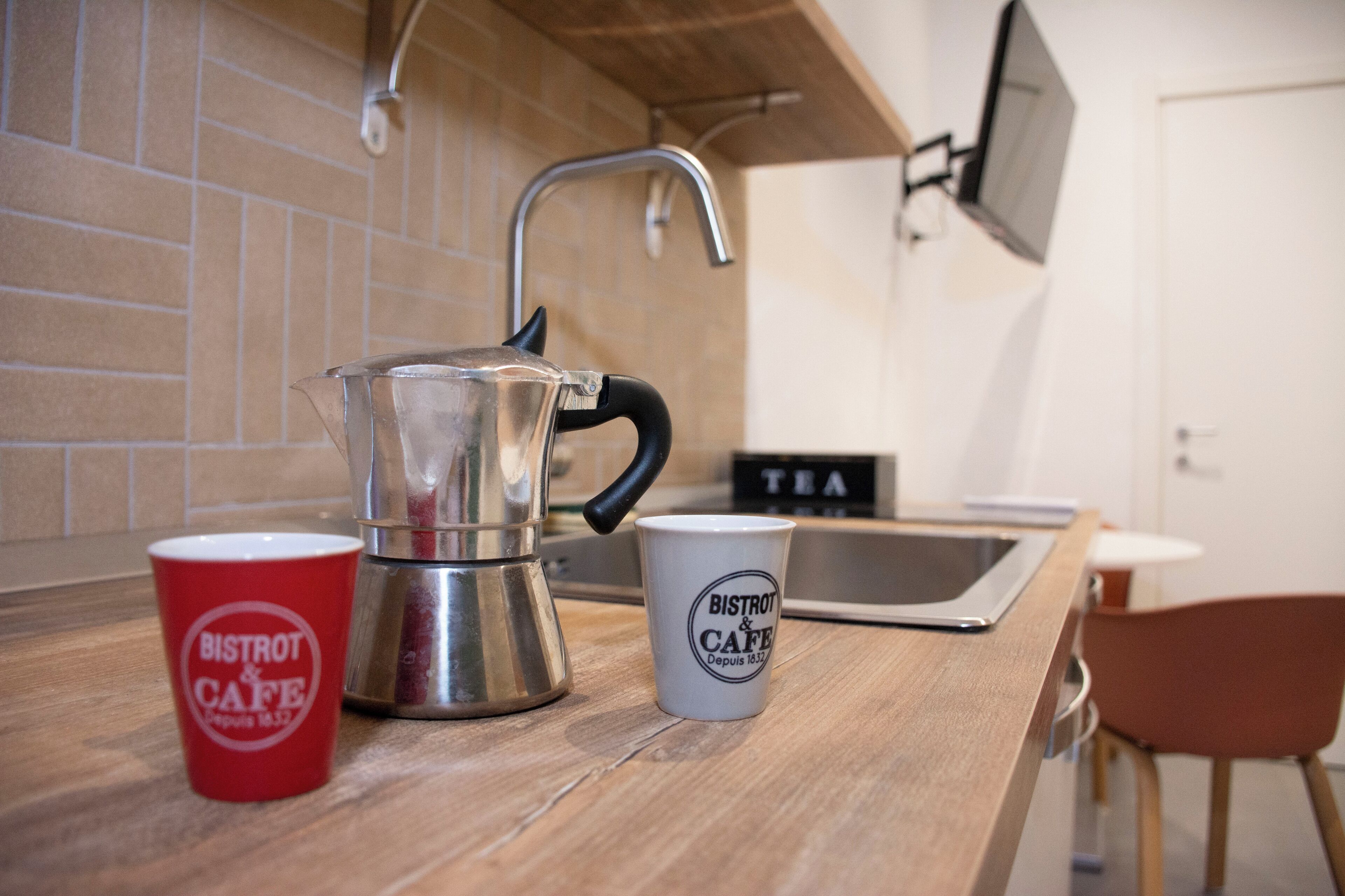 A kitchen with a coffee maker, a red cup, and a white cup with "BISTROT & CAFE" text.