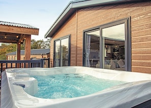 A hot tub on a wooden deck with a glass door leading to a patio area. - 2 bedroom accommodation in Bala, (Bala,)