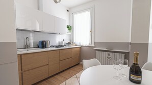 Une cuisine moderne avec des meubles blancs, un plan de travail en bois et un coin repas comprenant une table et deux verres à vin.
