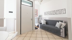 Un salon moderne avec un canapé gris, des coussins blancs, une lampe sur pied et une œuvre d’art murale.
