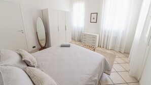 Une chambre à coucher comprenant un lit, une armoire, un miroir, une commode et une fenêtre avec des rideaux.