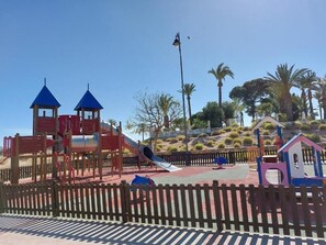 Ein Spielplatz mit Rutsche, Klettergerüsten und einem kleinen Haus-ähnlichen Bauwerk.