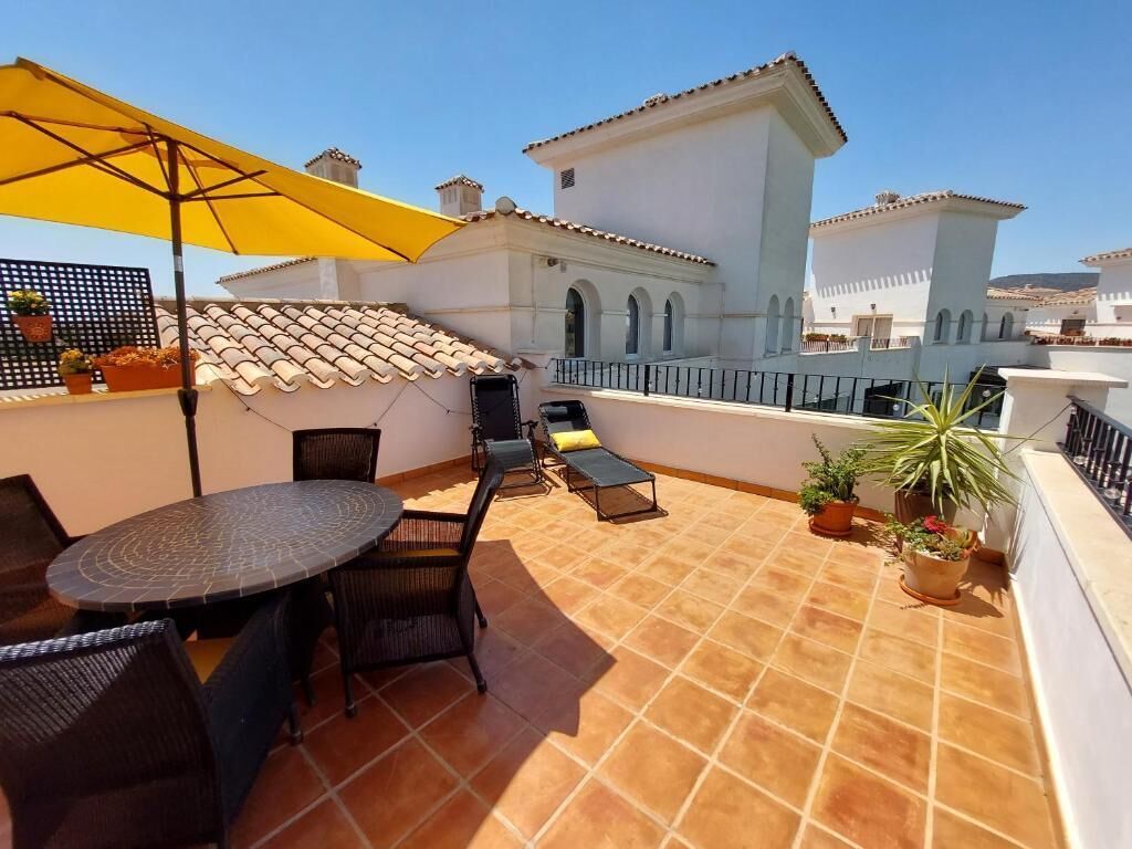 A rooftop terrace with a round table and chairs, a yellow umbrella, and potted plants.