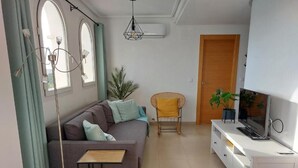 Uma sala de estar moderna com um sofá, uma mesinha, um painel para TV e uma cadeira.