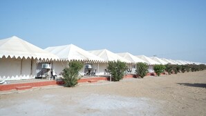 A row of white tents with red steps leading to the entrances, set in a sandy area with sparse vegetation. - Raj Dunes Resort (Jaisalmer)
