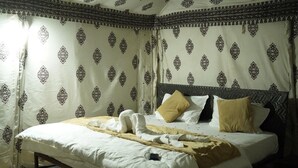 A neatly made bed with towels and a blanket, a headboard, and patterned curtains. - Raj Dunes Resort (Jaisalmer)