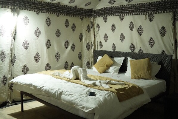 A neatly made bed with towels and a blanket, a headboard, and patterned curtains. - Raj Dunes Resort (Jaisalmer)