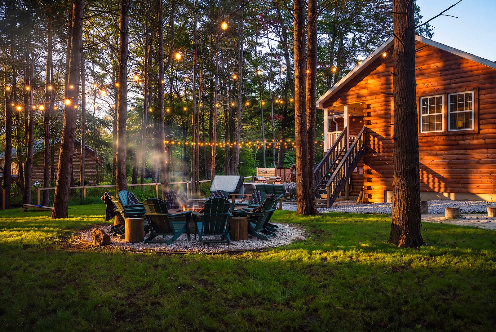 A log cabin with a fire pit and outdoor seating area surrounded by trees.