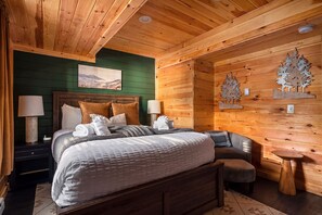 A wooden cabin bedroom with a bed, bedside tables, a nightstand, a bench, and wall decorations. - Sleeps 18 Luxury 8BR Cabin Hot Tub, Sauna & Game Room (Blakeslee)