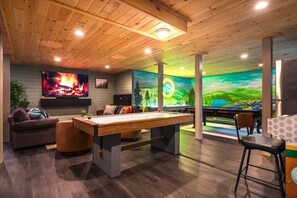 A room with a pool table, a sofa, a TV, and a mural. - Sleeps 18 Luxury 8BR Cabin Hot Tub, Sauna & Game Room (Blakeslee)