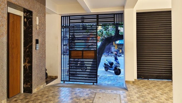 A modern entrance with a checkered floor, a wooden door, a black metal gate, and a closed roller shutter. - Seaa Breeze (Puducherry)