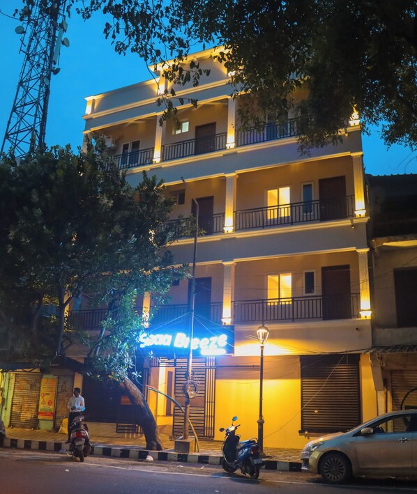 A multi-story building with balconies, a sign reading "Sana Breeze," and a parked scooter and car on the street.