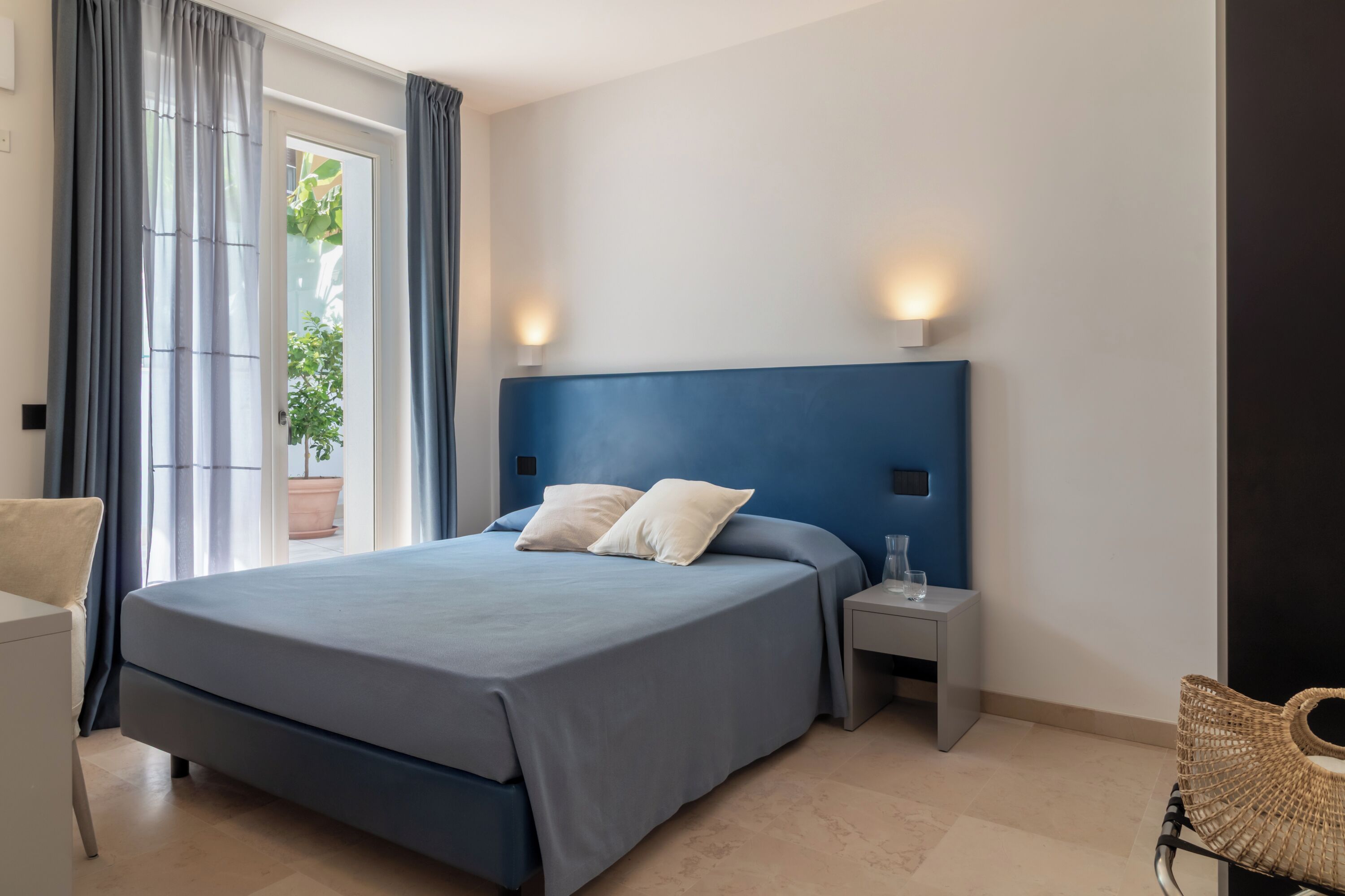 Un dormitorio con una cama grande, dos mesitas de noche, una lámpara de noche, una silla y una ventana con cortinas.