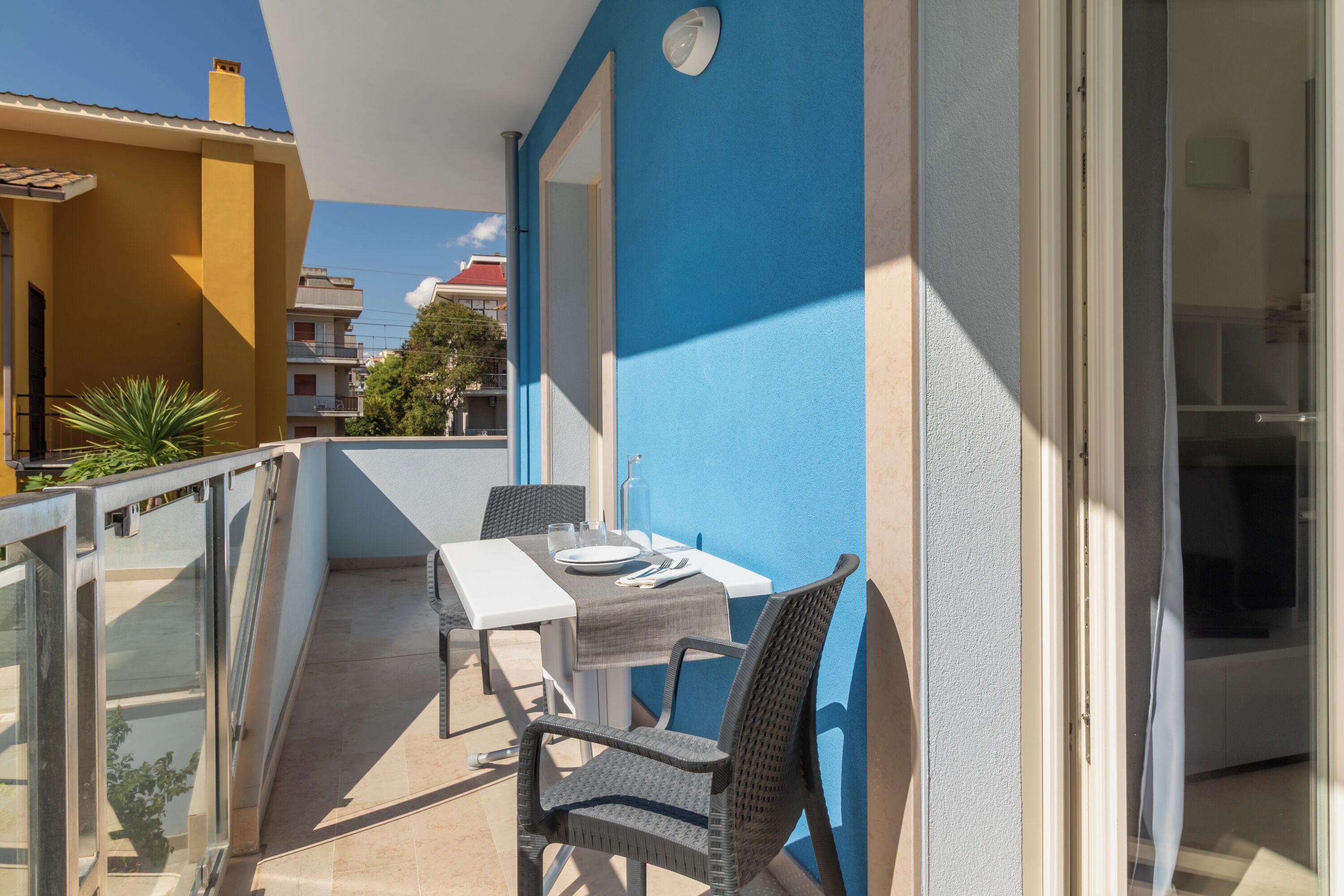A balcony with a table and chairs, a glass railing, and a view of neighboring buildings.