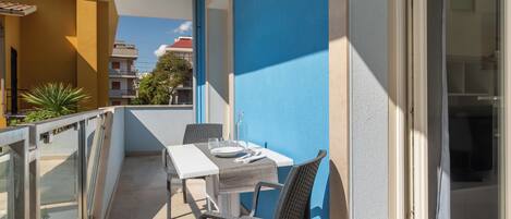 A balcony with a table and chairs, a glass railing, and a view of neighboring buildings.