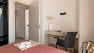 A hotel room with a bed, a desk, a chair, and a small table with a vase of dried flowers.