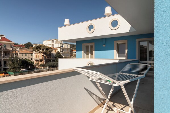 A balcony with a white folding chair and a small table, overlooking a residential area with houses and trees.