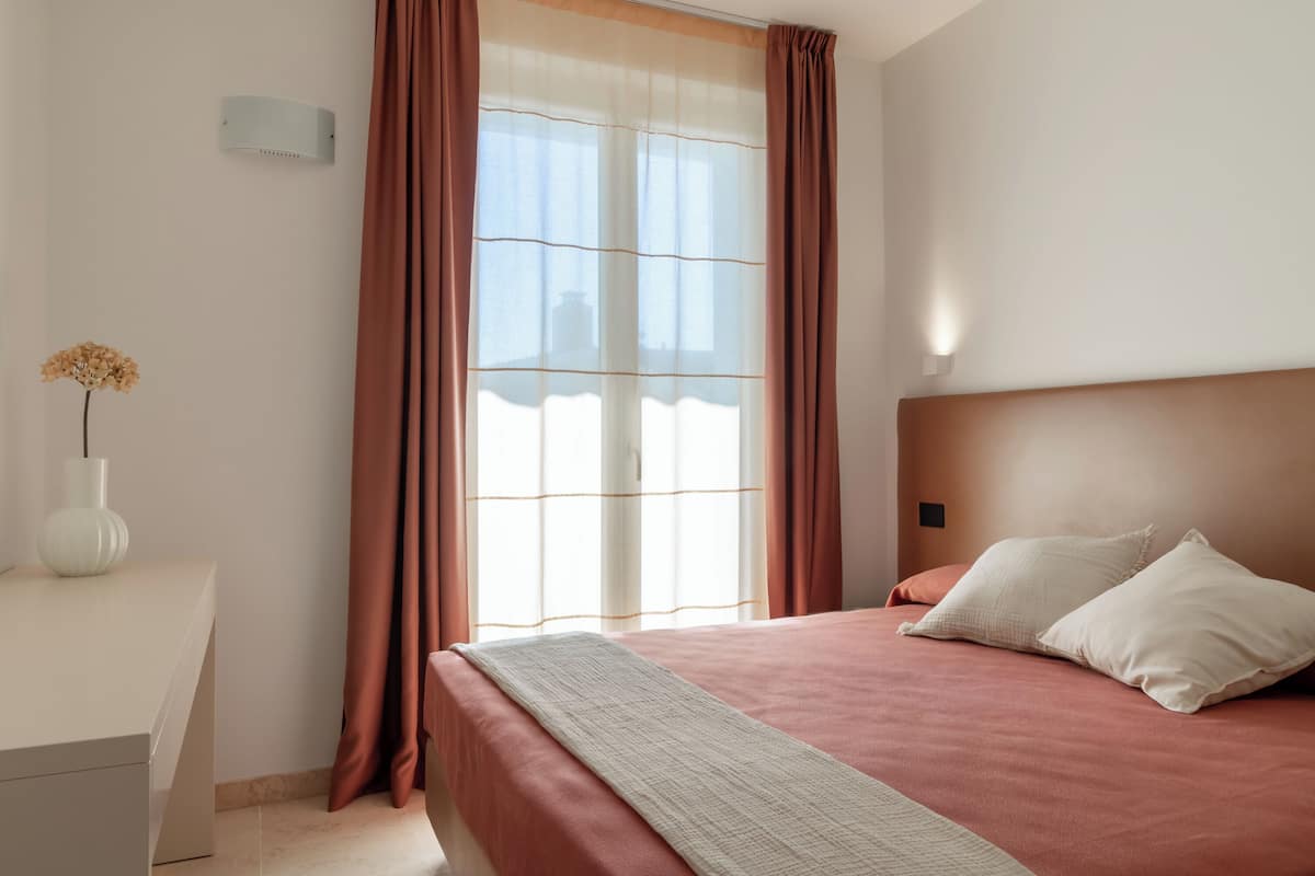 Ein ordentlich eingerichtetes Schlafzimmer mit einem Bett, Kissen, einem Nachttisch und einer Blumenvase.