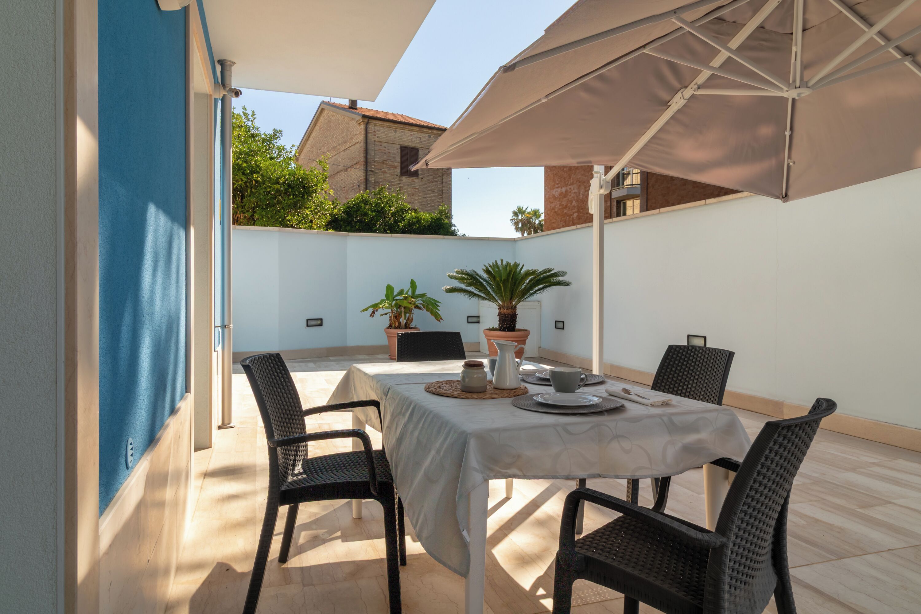 An outdoor patio with a table set for four, surrounded by chairs, under a large umbrella.