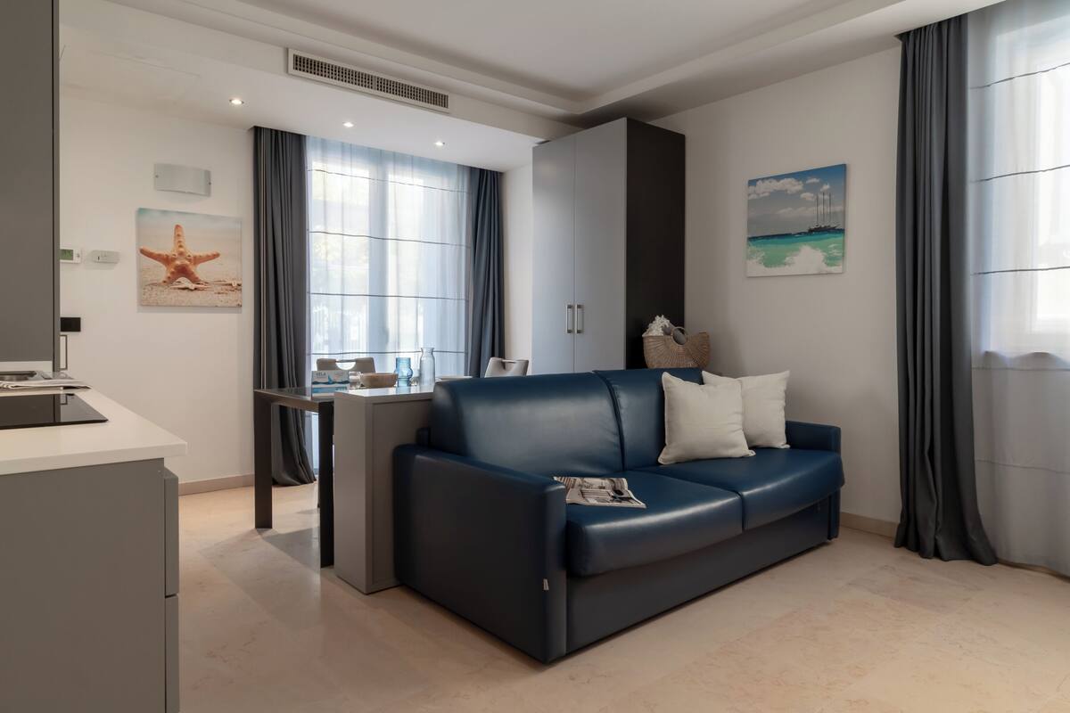 Ein modernes Wohnzimmer mit einem dunkelblauen Sofa, einer kleinen Küchenzeile und einem Esstisch.