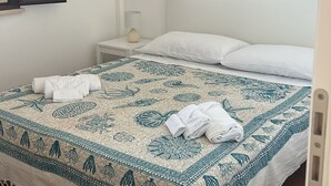 A bedroom with a bed, a nightstand, a lamp, a mirror, and a window with curtains. - Villa Uzzo -Scopello (Sicilia)