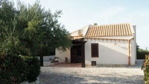 A small building with a tiled roof, a door, and a window. There is a paved area in front of the building. - Villa Uzzo -Scopello (Sicilia)