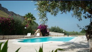 A swimming pool with white lounge chairs and a stone wall. - Villa Uzzo -Scopello (Sicilia)