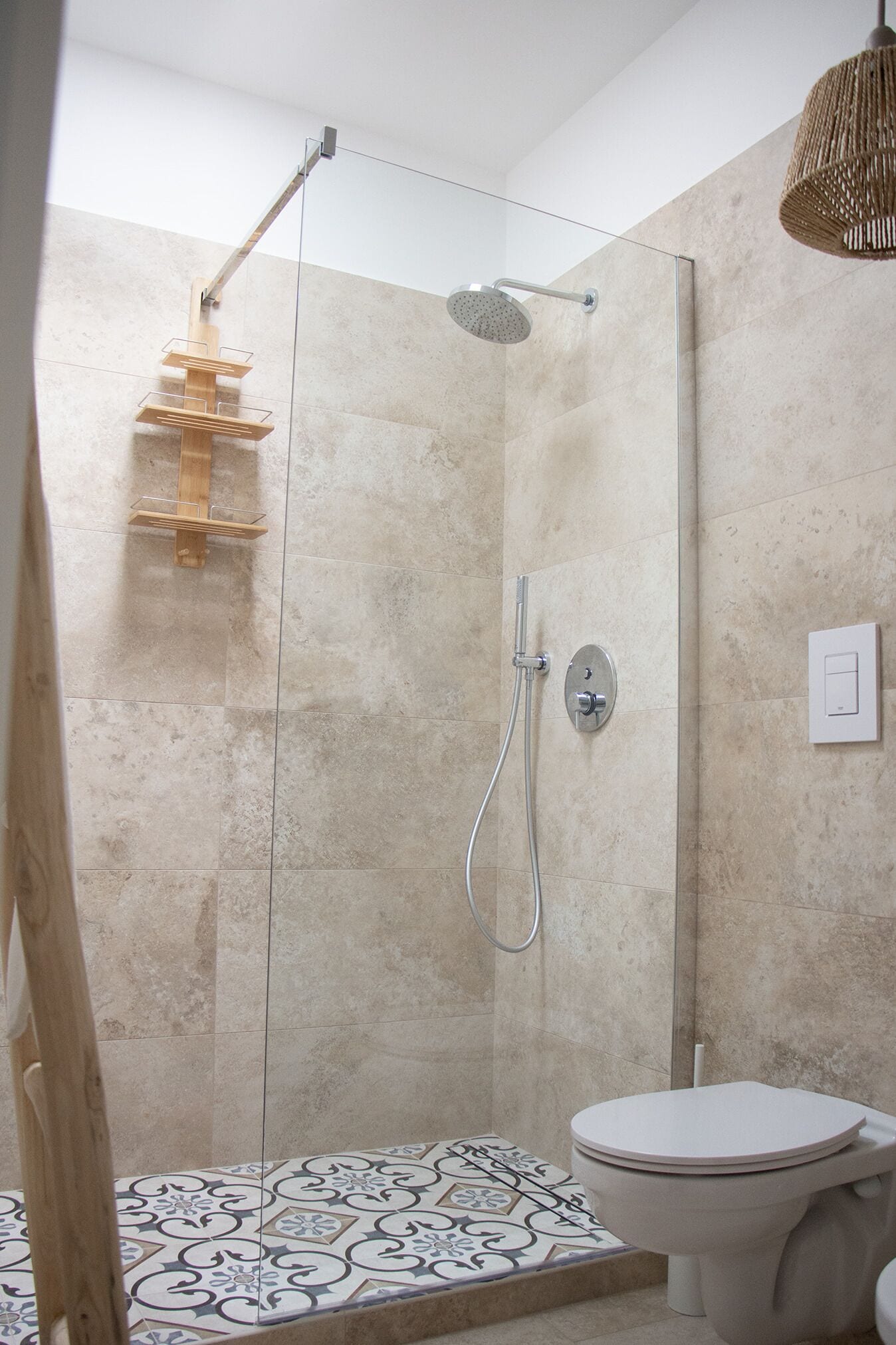 A shower with a glass door, a toilet, and a patterned floor.