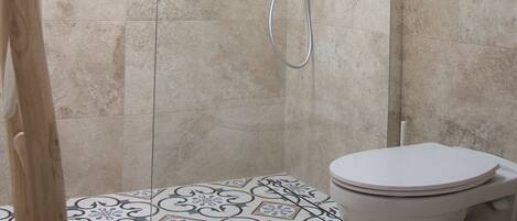 A shower with a glass door, a toilet, and a patterned floor.