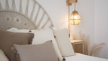 Un letto con testiera in macramè, diversi cuscini, una lampada a parete e un piccolo scaldino.