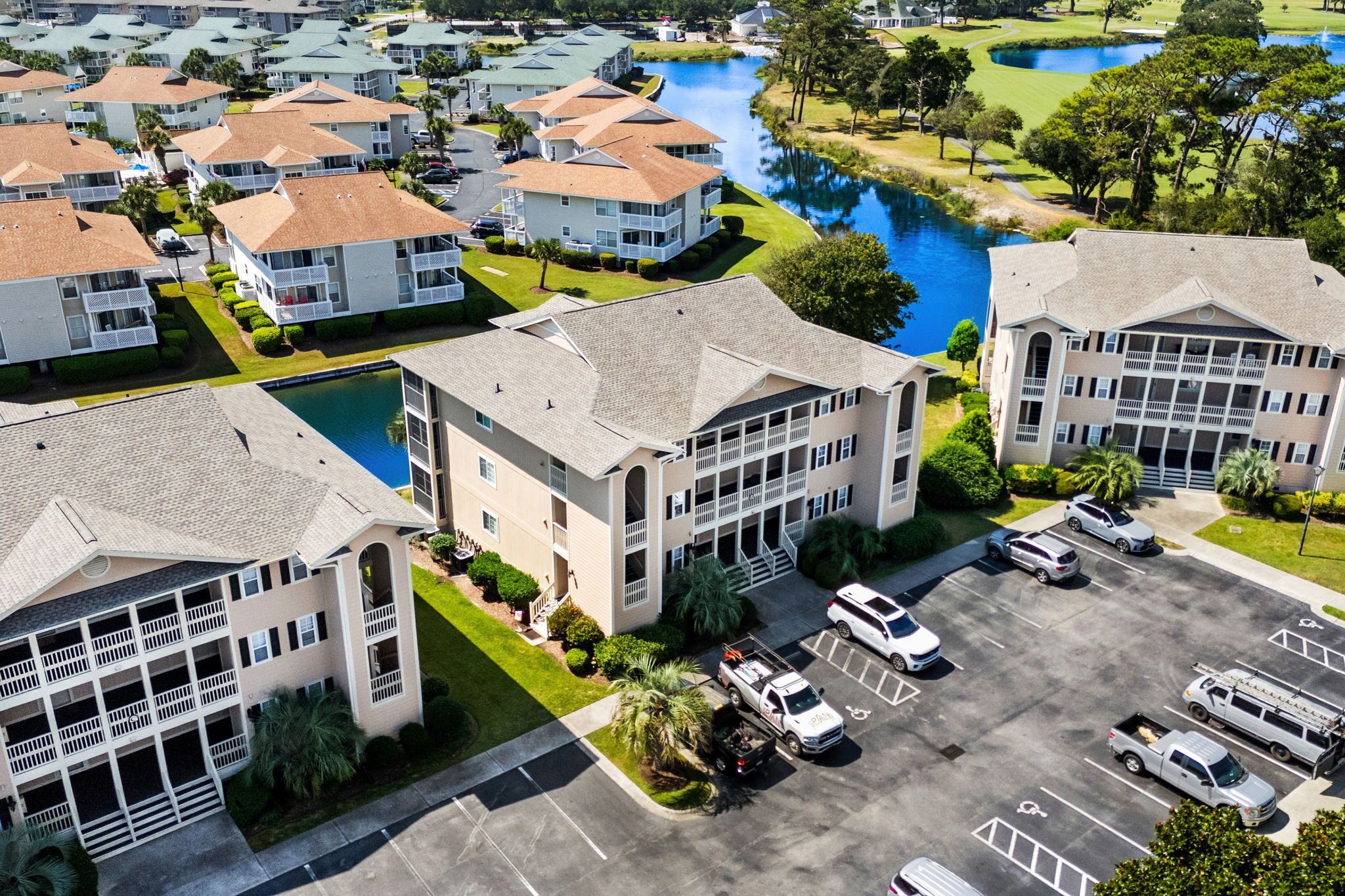 A multi-story residential building with a parking lot and a small lake.