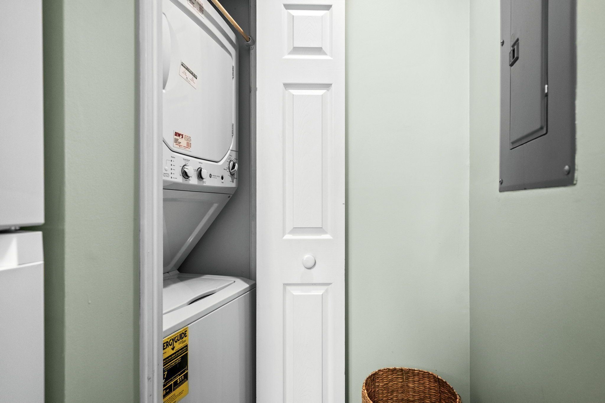 A laundry room with a washer and dryer, a white door, and a basket on the floor.