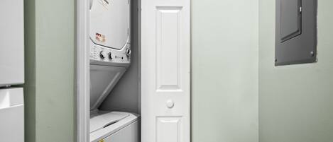 A laundry room with a washer and dryer, a white door, and a basket on the floor.