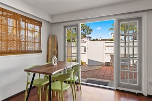 A dining area with a wooden table and green chairs, a bamboo blind, and a view through a glass door to an outdoor patio. - The Wave by Coastline Vacation Rentals (San Diego)