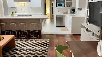 A modern kitchen with white cabinetry, a central island, bar stools, a dining table with chairs, and a television.