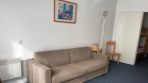 A living room with a sofa, a small wooden table, a chair, a radiator, and a door leading to another room. - Gourette Studio 4 pers, Slope View, WIFI, Pets (Gourette)
