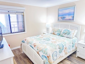 A bedroom with a bed, bedside tables, a window, and a painting on the wall. - Tilghman Beach and Racquet Club 306 (North Myrtle Beach)