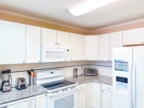 A kitchen with white cabinets, a microwave, a stove, a toaster, and a refrigerator. - Tilghman Beach and Racquet Club 306 (North Myrtle Beach)