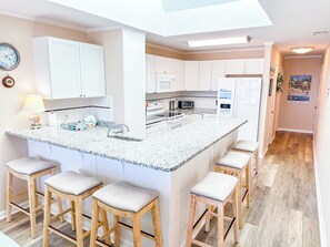 Eine moderne Küche mit weißen Schränken, einer Granit Arbeitsplatte und einer zentralen Kochinsel mit Barhocker.